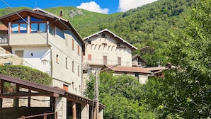 A traditional building with a balcony, a stone facade, and a view of a green hillside.