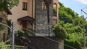 A two-story house with a stone facade, a balcony with a wrought iron railing, and a garden with pink flowers.