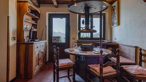 A rustic kitchen with wooden beams, a central stove, and a dining area with wooden chairs and a round table. - Arte e Cucina by Interhome (Gravedona)
