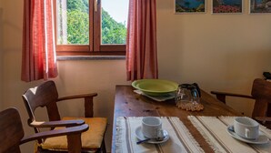 Ein Essbereich mit einem Holztisch, Stühlen, einer grünen Schüssel, zwei weißen Tassen und einer Kaffeekanne.