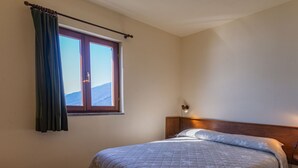 Ein Schlafzimmer mit einem Bett, einem Fenster mit Vorhängen, einem Nachttisch und einer Wandlampe.
