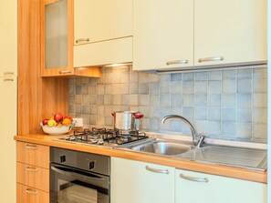 Une cuisine équipée d’une cuisinière à gaz, d’un évier et d’un saladier rempli de fruits posé sur le plan de travail.