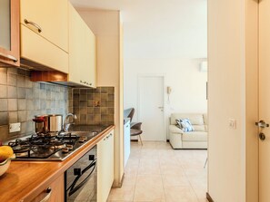 Une cuisine moderne équipée d’une cuisinière, d’un évier et de placards, qui donne sur un espace de vie comprenant un canapé et une porte.