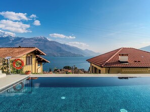 Une piscine avec vue sur la montagne, une bouée de sauvetage et un bâtiment avec un toit en tuiles.