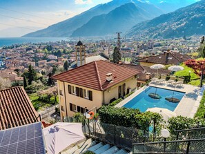 Un immeuble résidentiel doté d’une piscine, entouré d’un jardin luxuriant et offrant une vue sur la ville et les montagnes.