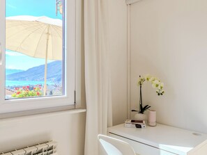 Ein Zimmer mit Fensterblick auf einen Strand, ein Schreibtisch mit Blumenvase und eine Heizung.