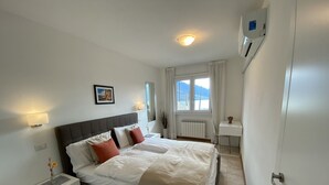 A neatly arranged bedroom with a bed, bedside table, lamp, and a view of the outdoors.