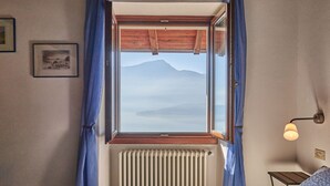 Een slaapkamer met een groot raam, een radiator, een nachtkastje en een lamp.