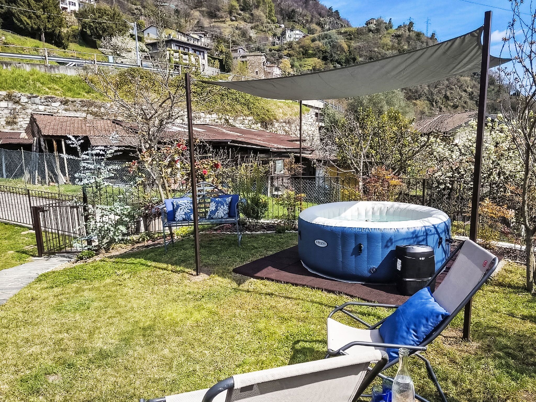 A backyard with a hot tub, a lawn chair, and a table with a bottle.