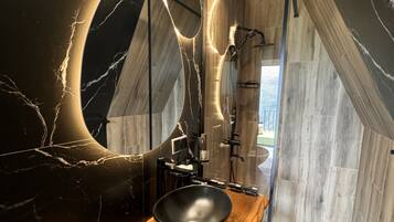 Un baño moderno con un espejo grande, un lavabo negro y suelo de madera.