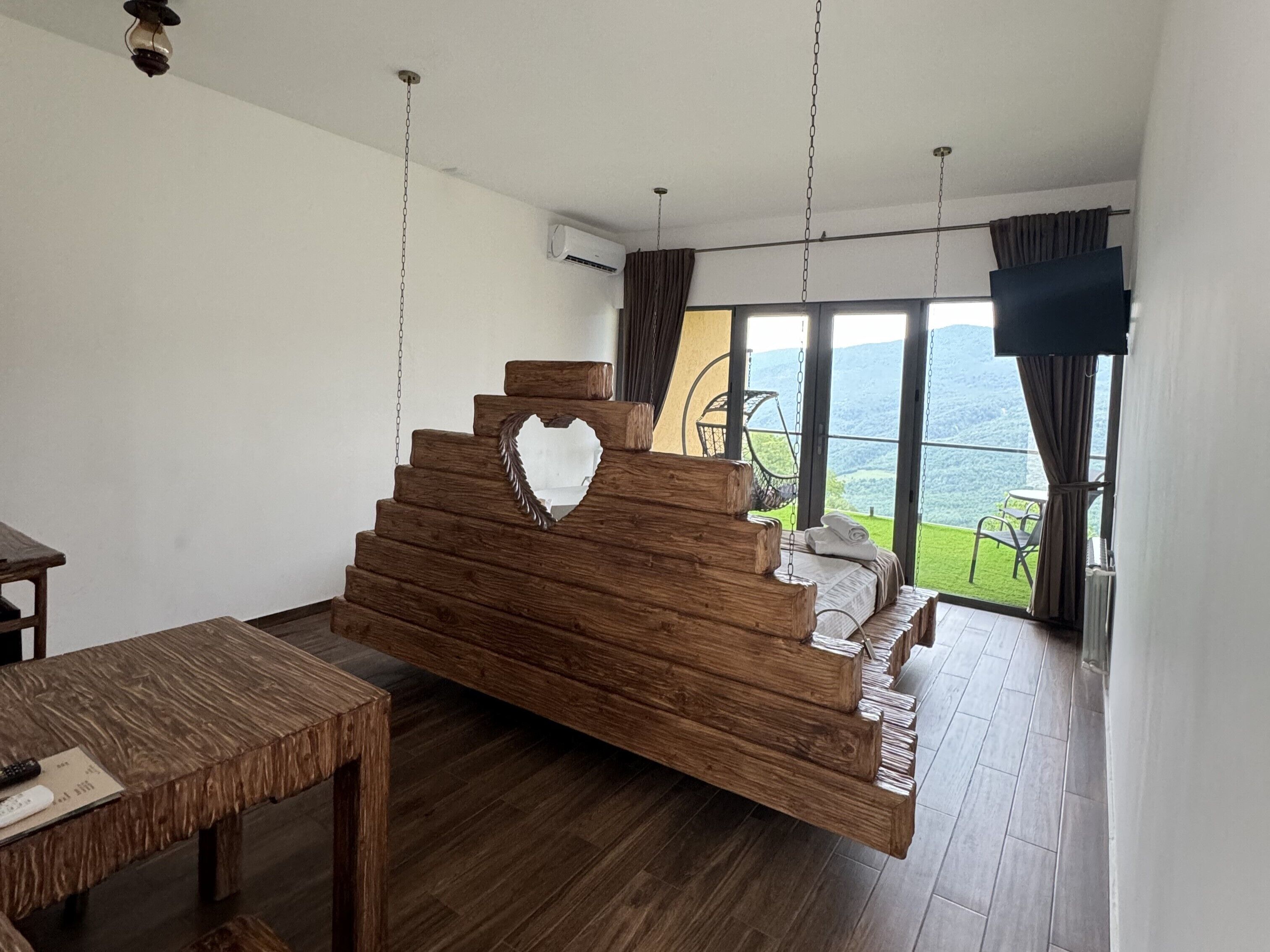 A modern room with a wooden bed, a dining table, and a view of the outdoors.