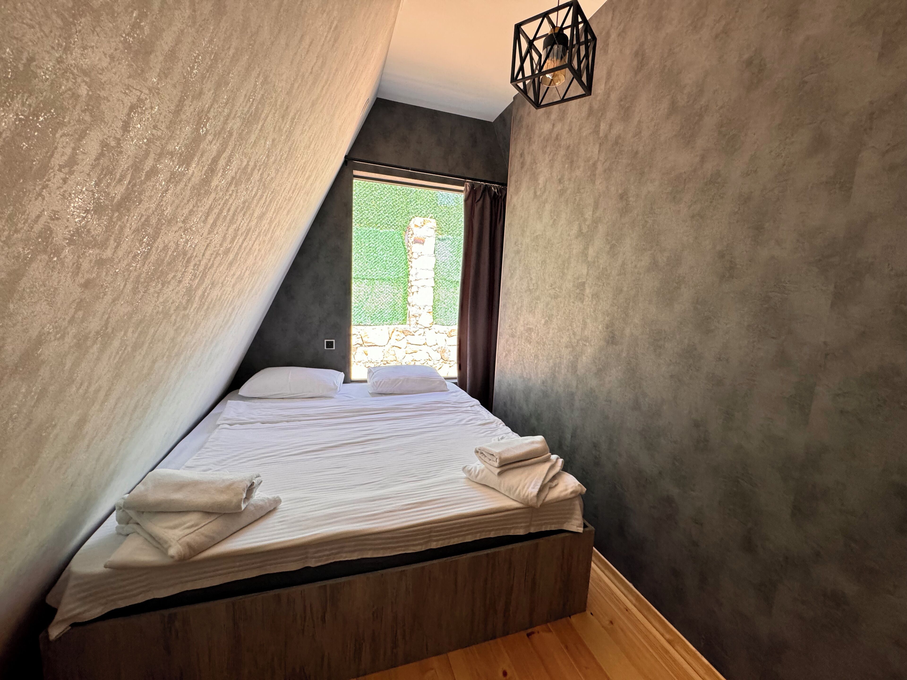 Une chambre avec un plafond en pente, un lit recouvert de draps blancs et une vue sur la verdure à l’extérieur.