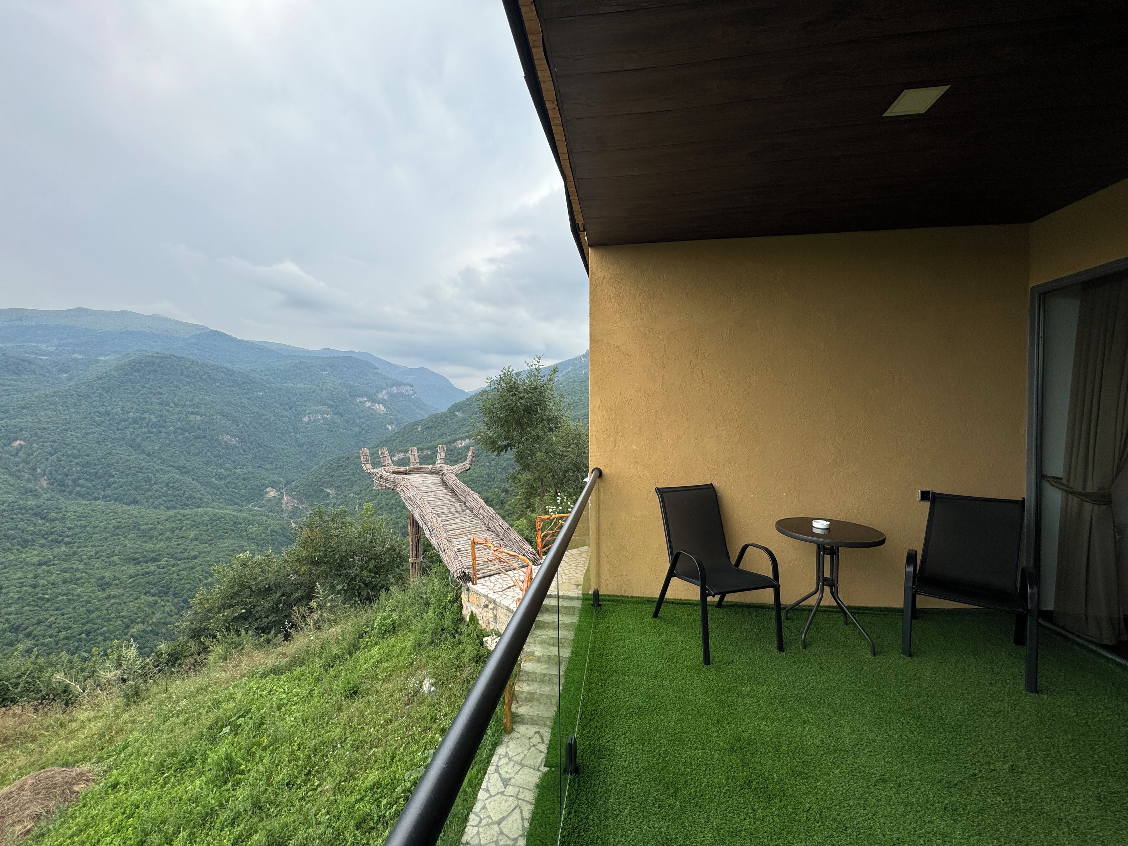 A balcony with a view of a mountain range, two chairs, and a small table.