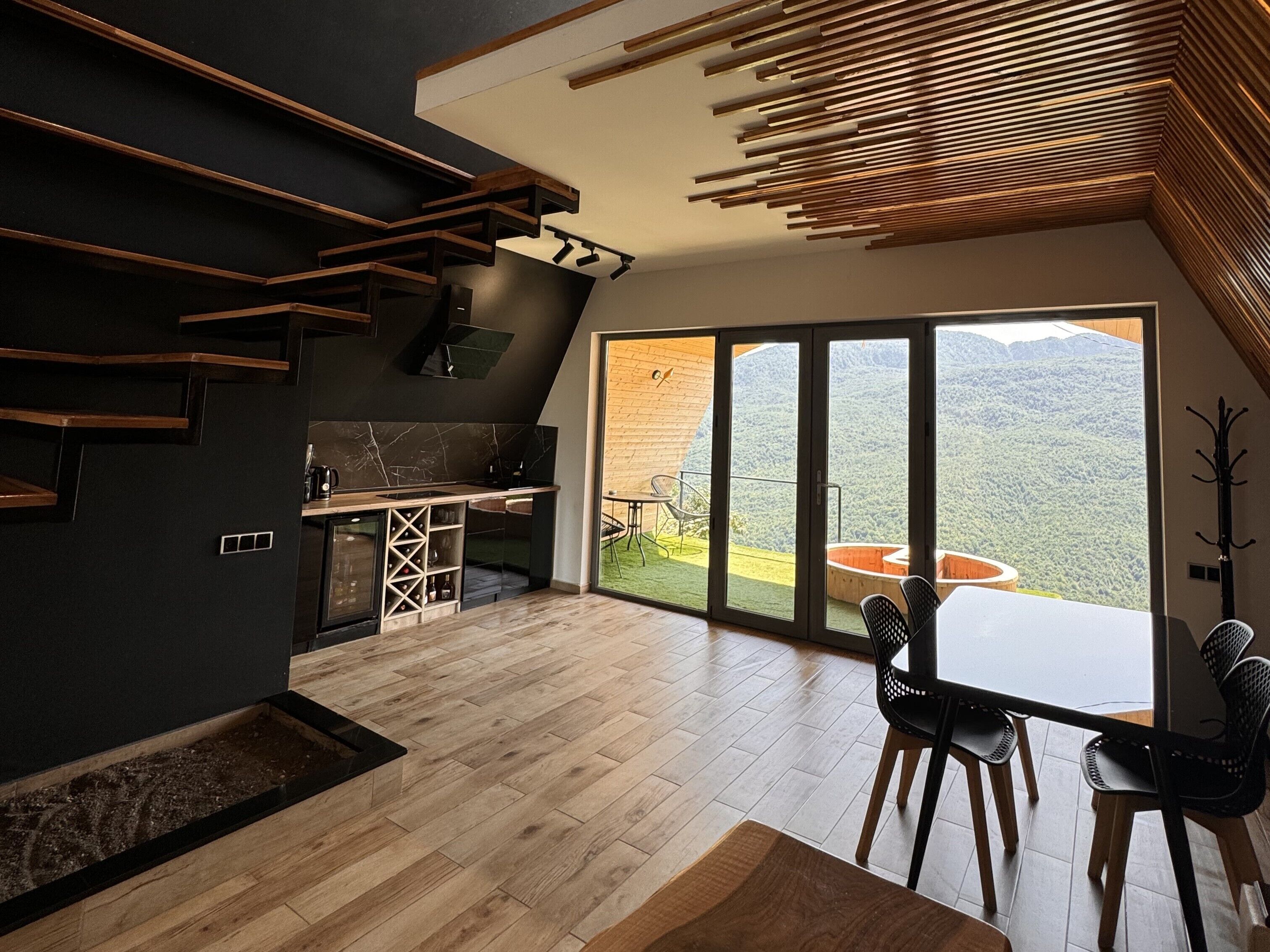 Een moderne keuken met een ingebouwde wijnrek, een eethoek met een tafel en stoelen, en een grote schuifdeur naar een balkon met uitzicht op de bergen.