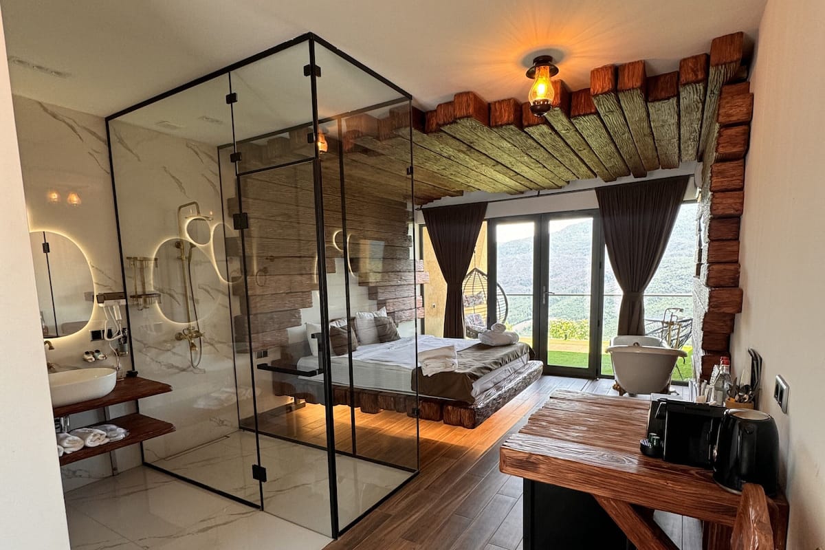 A modern bathroom with a glass partition, a wooden bench, and a large window overlooking a scenic view.