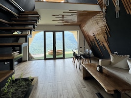 Un interior moderno con una escalera de madera, una zona de comedor de cristal y vistas a un paisaje montañoso.