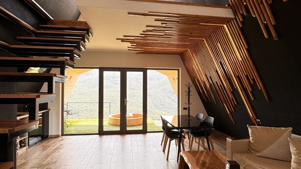 A modern interior with a wooden staircase, a dining area, and a large sliding glass door leading to a garden. - Lost in Sky (Yenokavan)