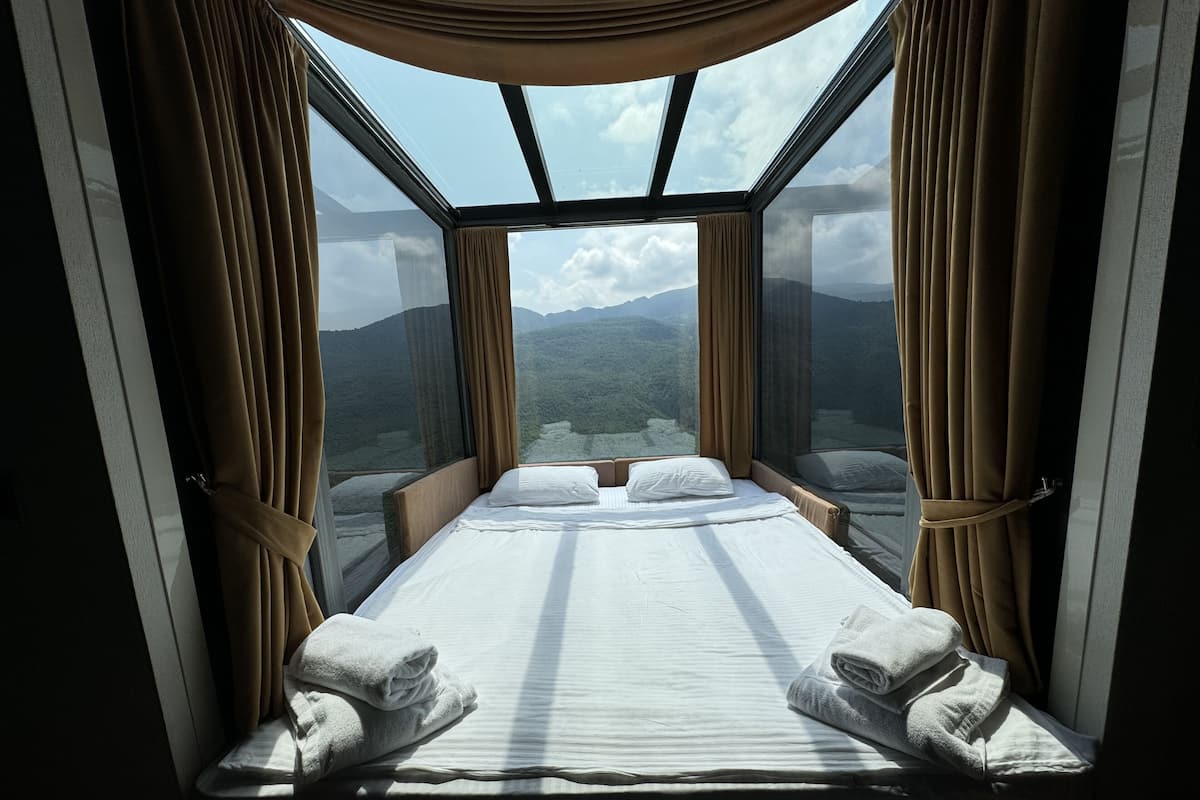 A room with a bed, curtains, and a view of mountains.