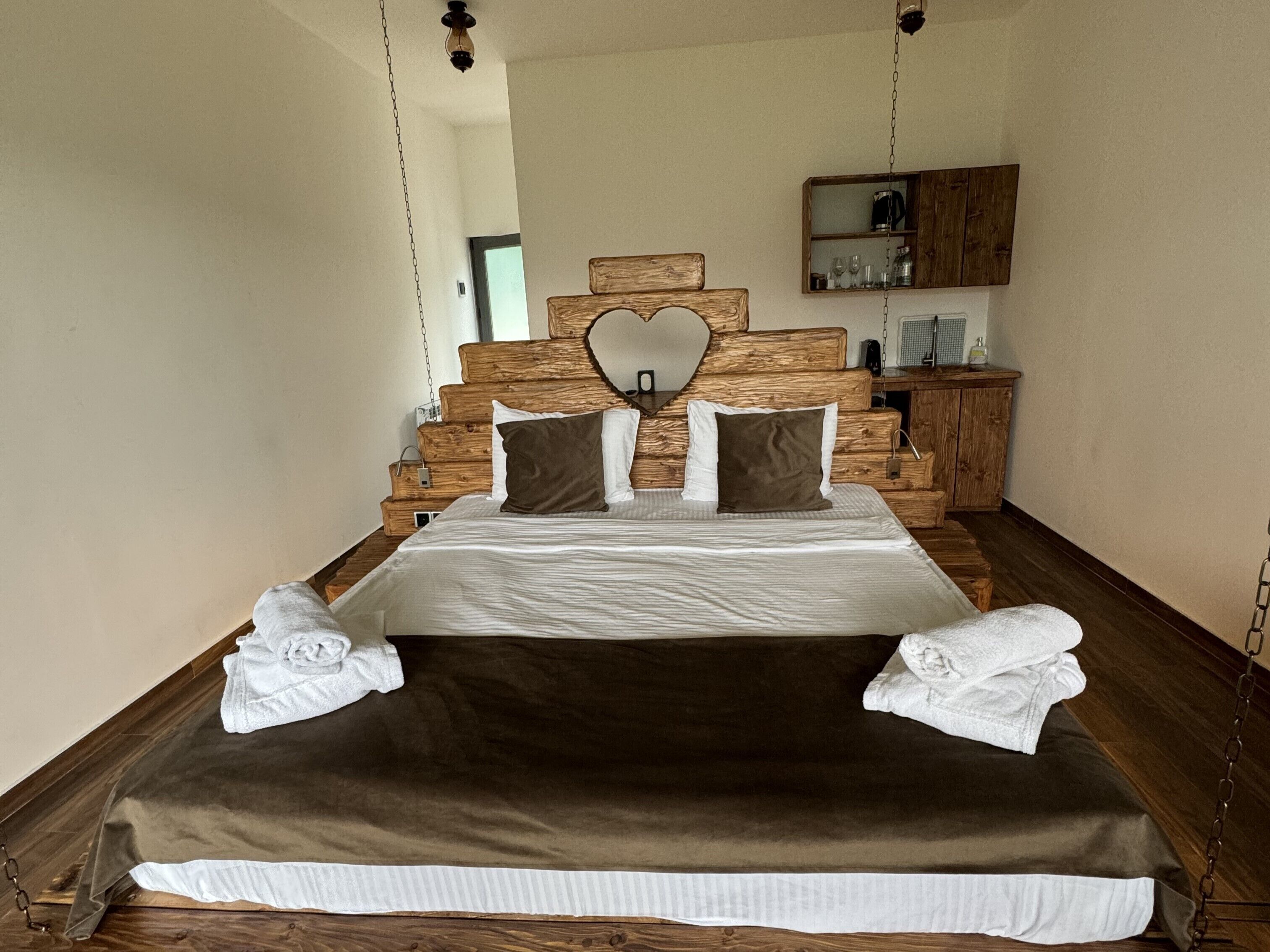 A bedroom with a large bed, wooden headboard, and a heart-shaped mirror.