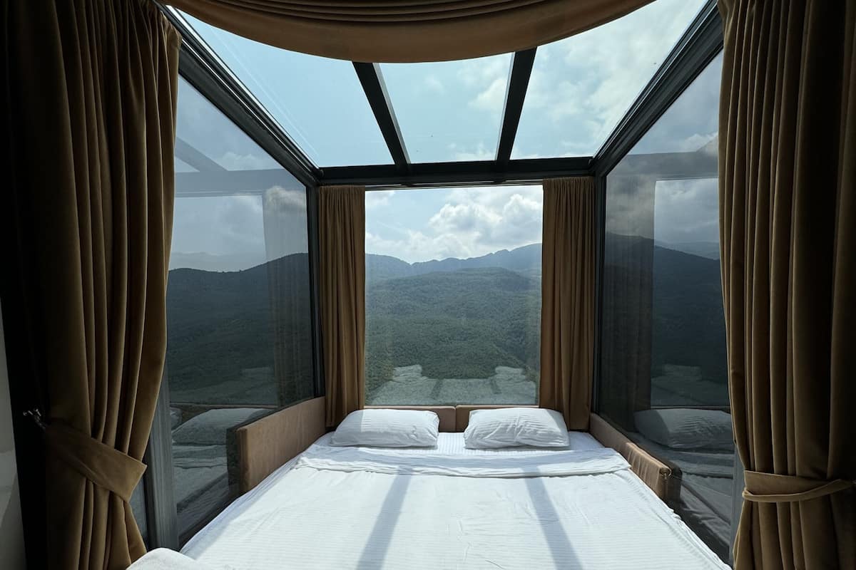 A bedroom with a large bed, two pillows, and a view of mountains through a large window.