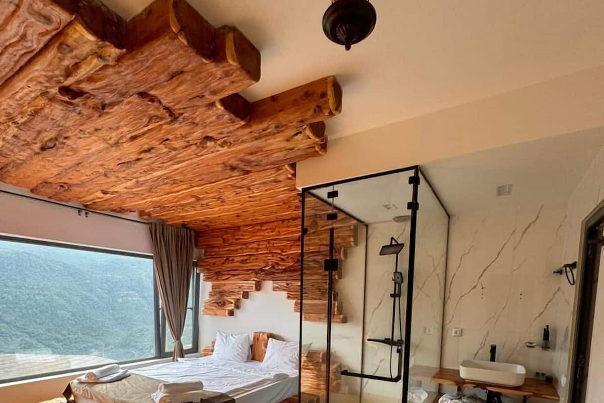 A bedroom with a wooden bed, a glass shower enclosure, and a view of the outdoors.