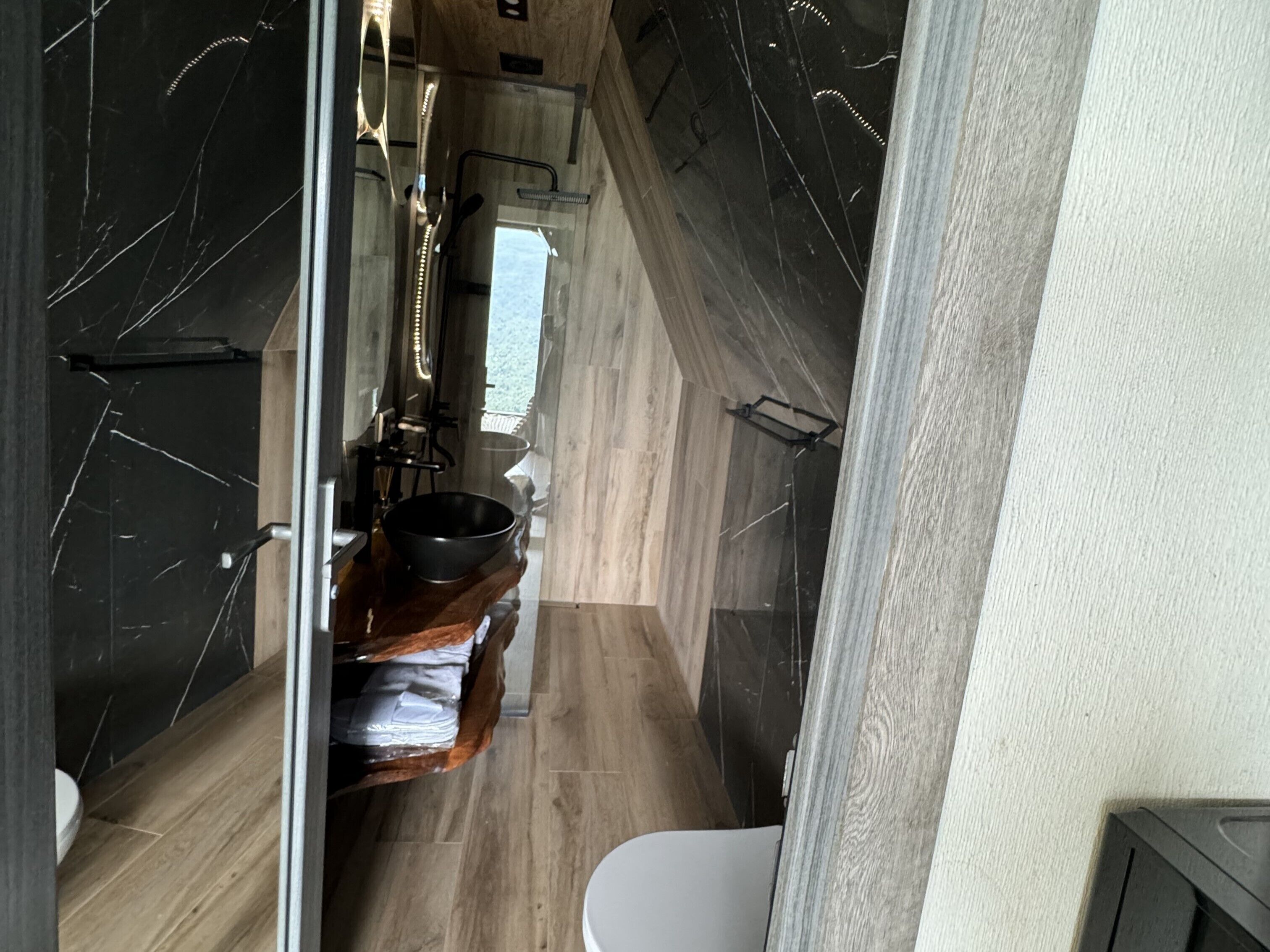 A narrow bathroom with a wooden vanity, a black sink, and a white toilet.