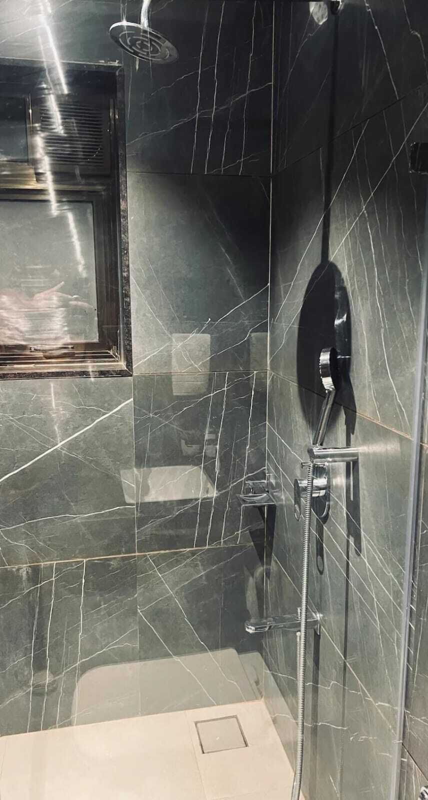 Un baño con cabina de ducha de vidrio, un cabezal de ducha de mano y un grifo empotrado en la pared.