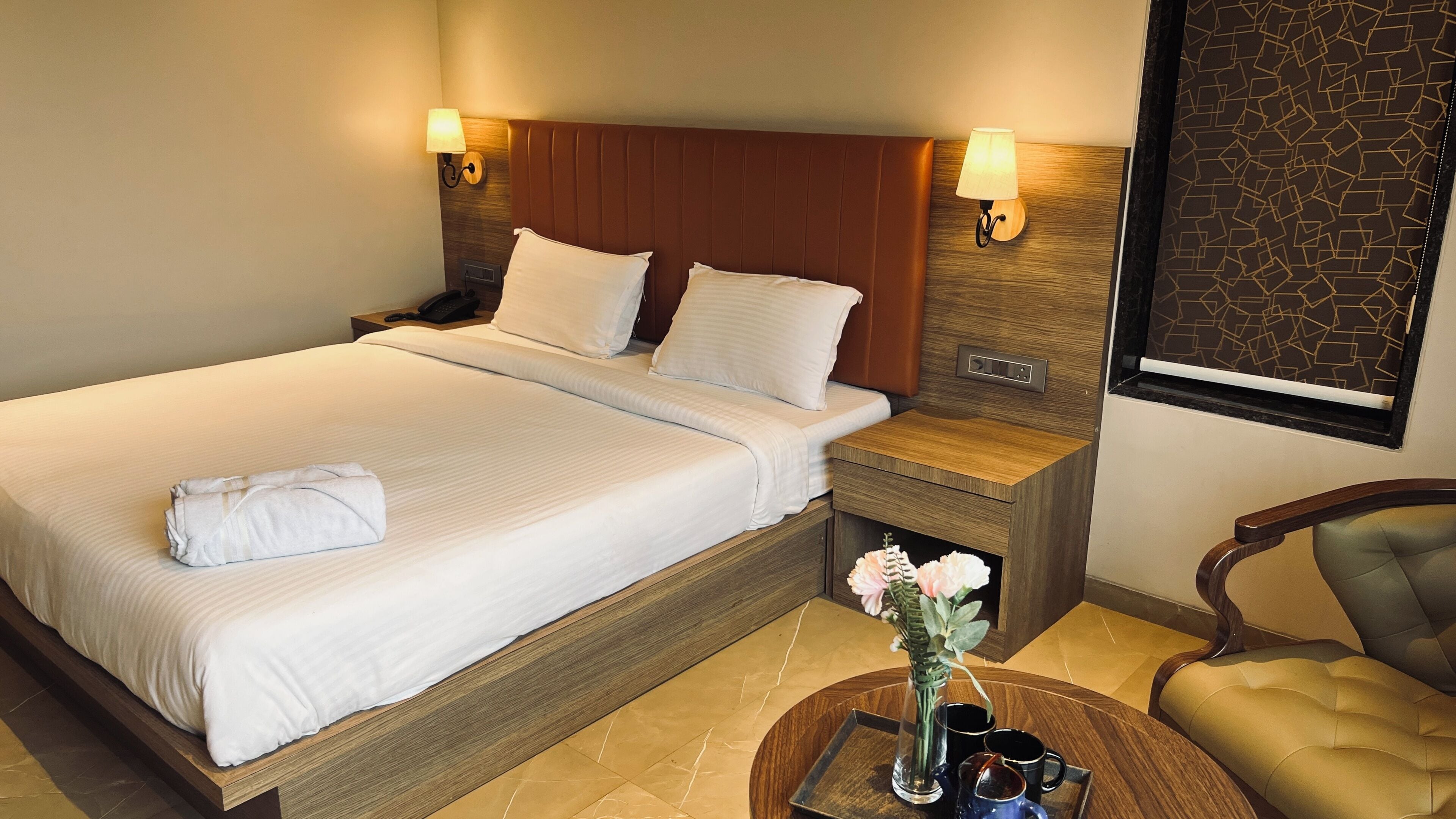 A hotel room with a large bed, bedside tables, a chair, and a vase with flowers.