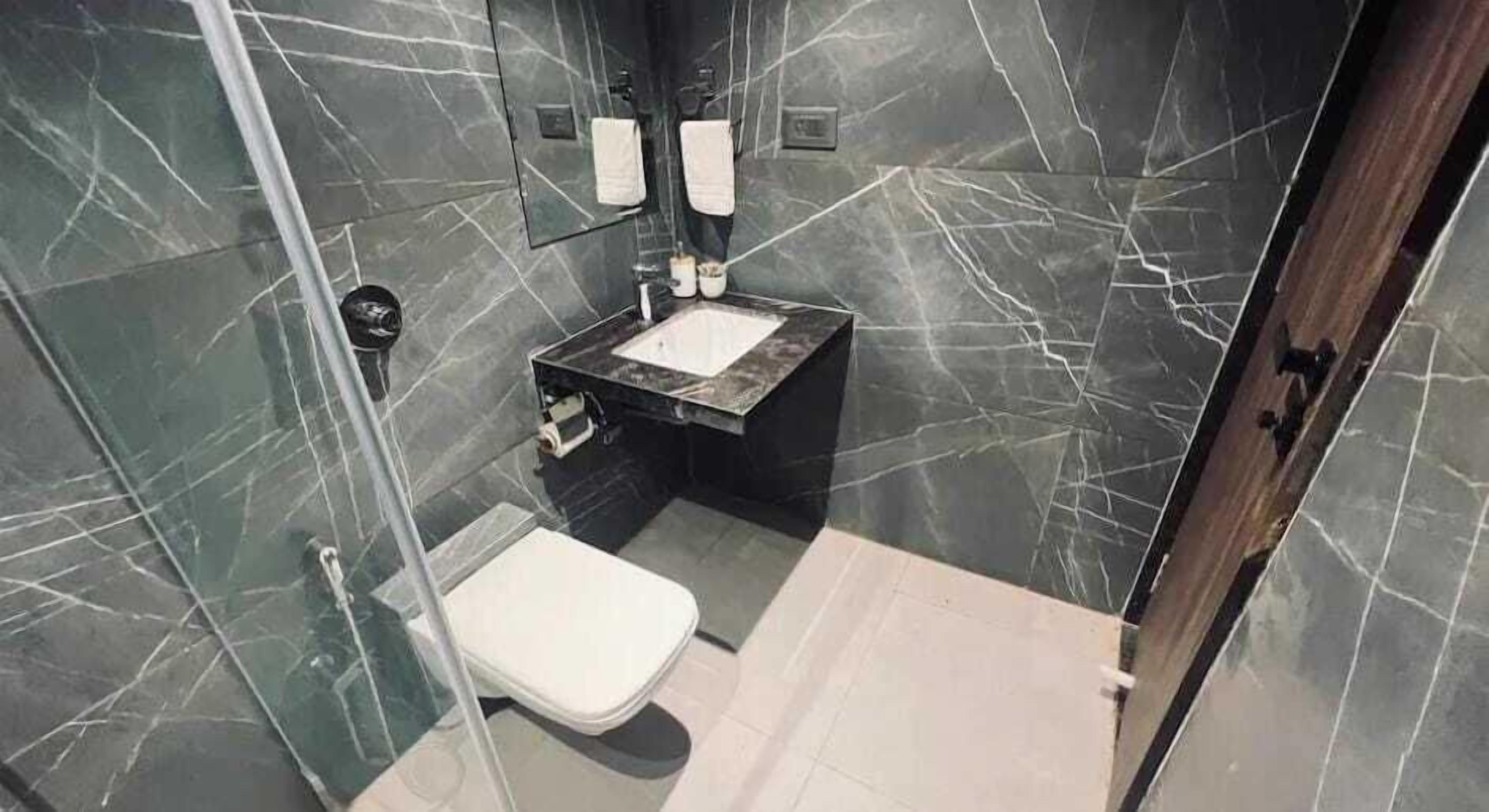 A bathroom with a marble wall, a sink, a toilet, and a mirror.