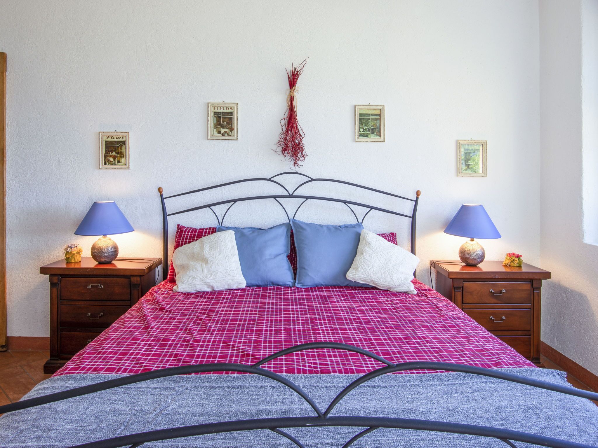 A neatly made bed with a checkered bedspread, two bedside tables with lamps, and a wall with framed pictures.
