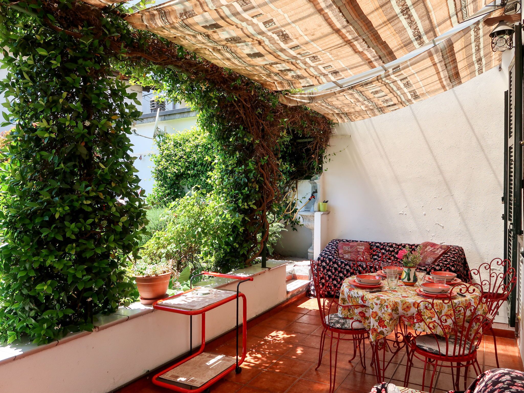Eine Terrasse mit Esstisch, umgeben von Topfpflanzen und einem roten Metallstuhl.