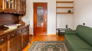 A living room with a wooden cabinet, a green sofa, a patterned rug, and a door with a frosted glass panel. - Assunta by Interhome (Dongo)