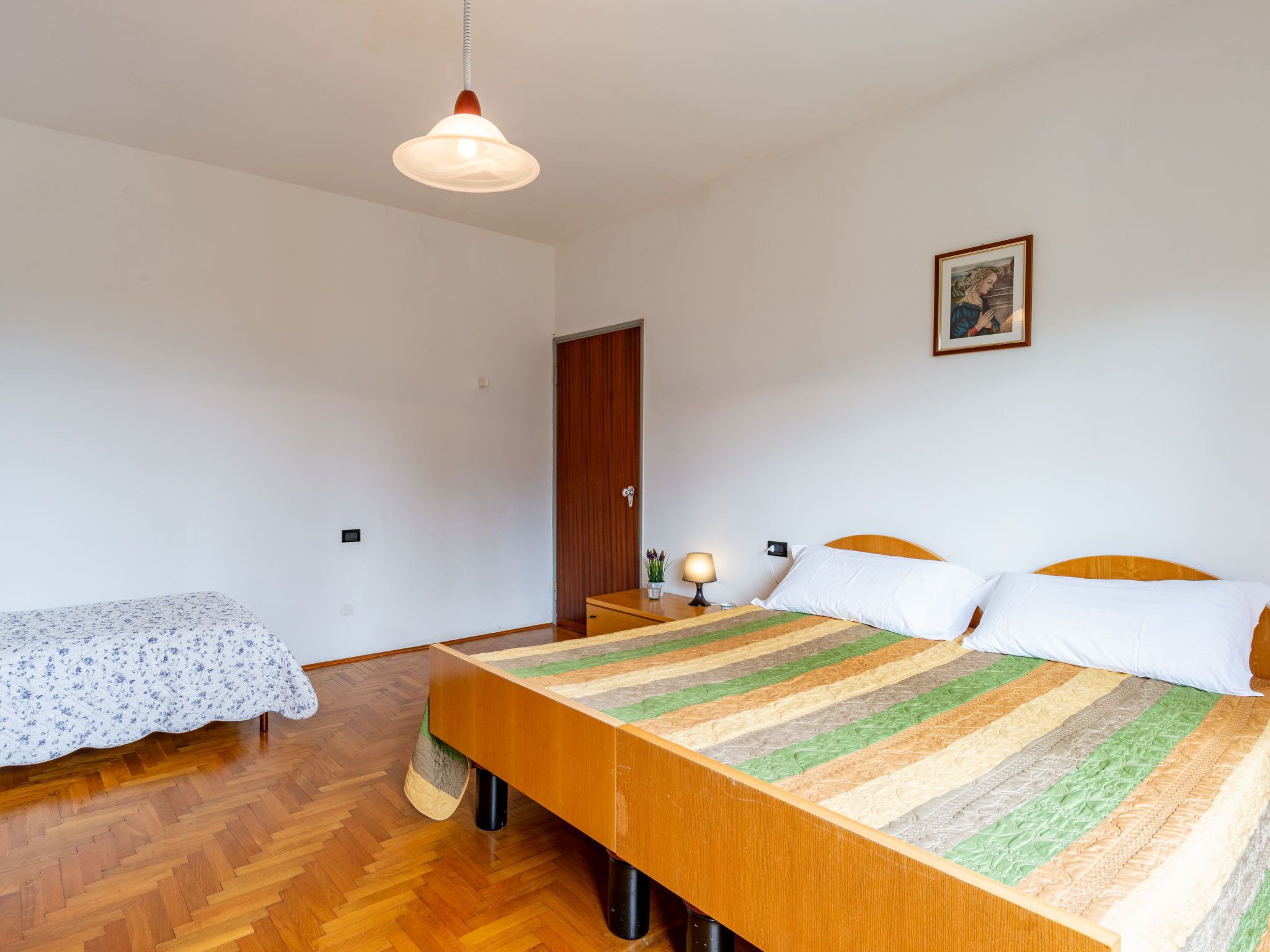 A bedroom with a wooden bed, a nightstand, a lamp, a door, and a small table with a plant.