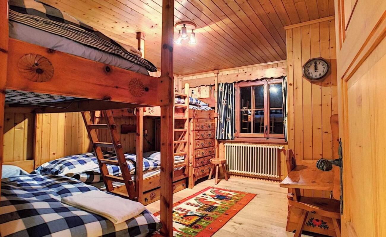 Een slaapkamer in een houten chalet met stapelbedden, een houten ladder, een dressoir, een radiator en een klok aan de muur.