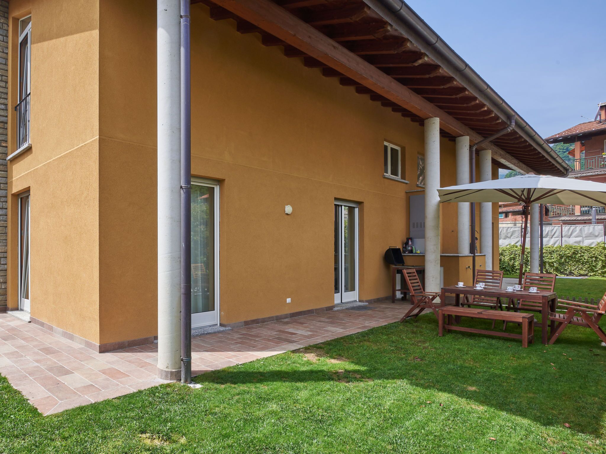 A building with a yellow exterior, a covered patio with a table and chairs, and a grassy lawn.