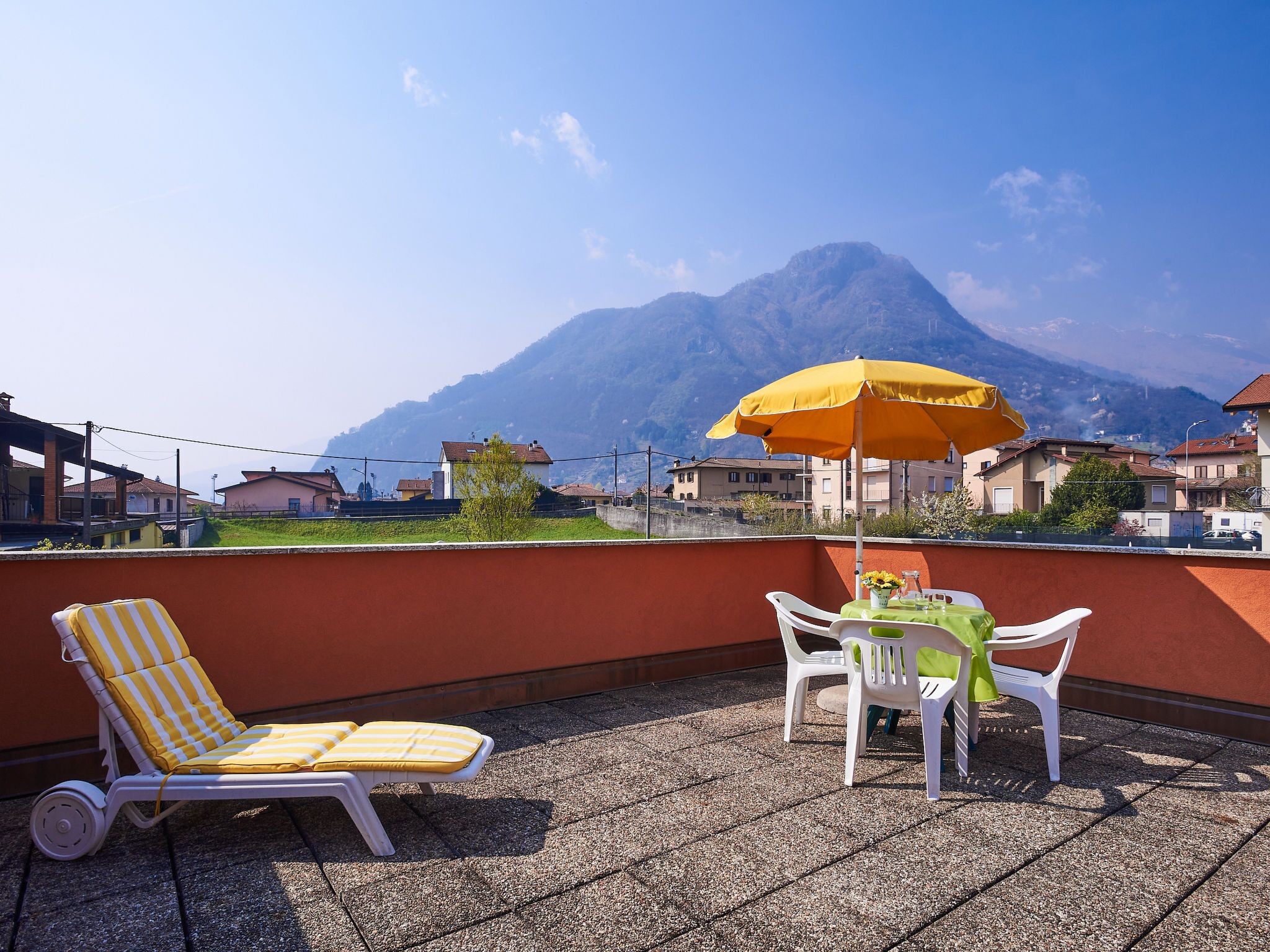 Een terras met een loungestoel met gele strepen, een tafel met een gele parasol en uitzicht op een berg.