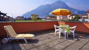 Una terraza con una silla de lounge a rayas amarillas, una mesa con sombrilla amarilla y vistas a la montaña.