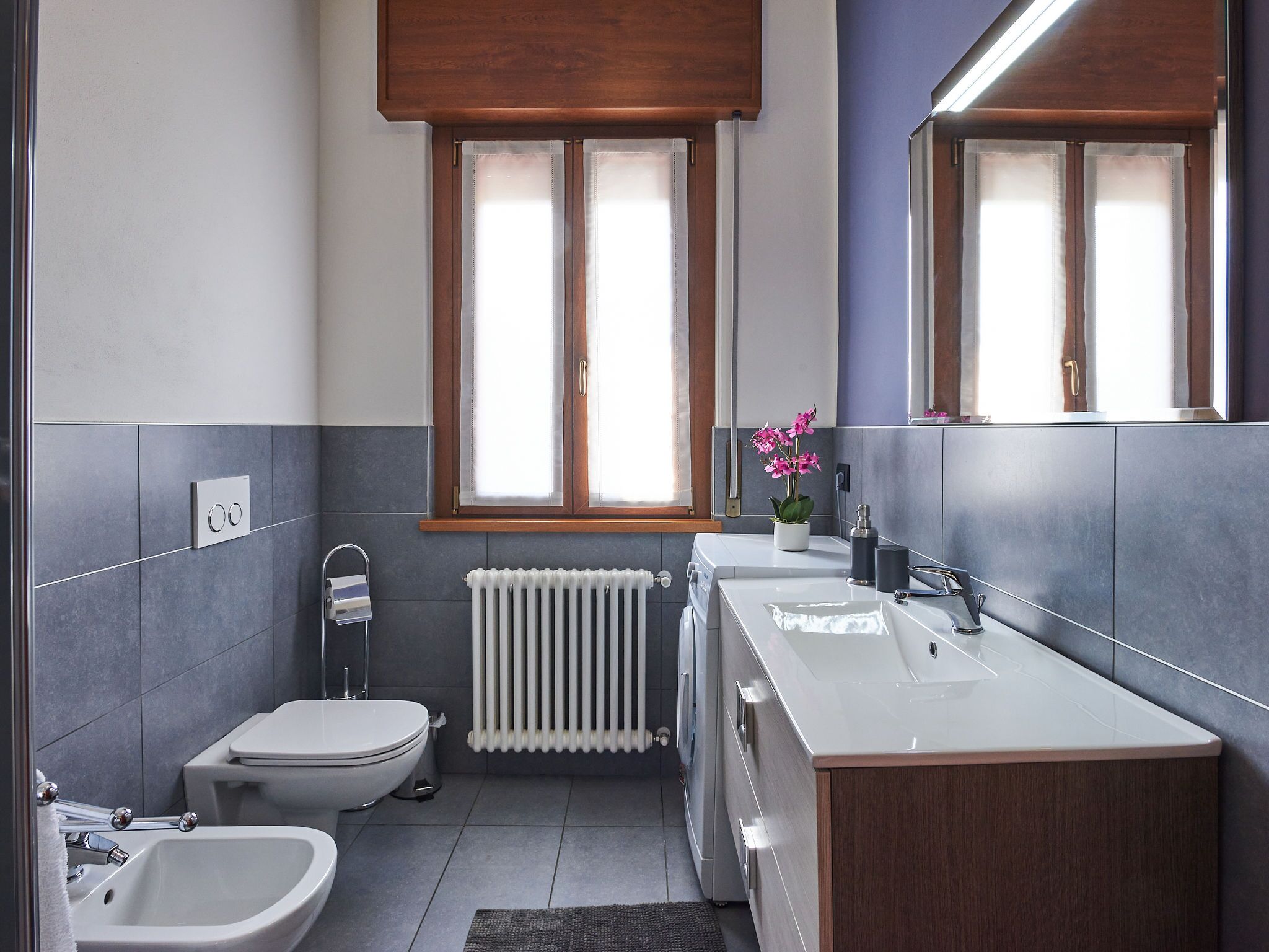 A modern bathroom with a toilet, bidet, sink, and mirror.
