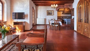 Ein geräumiges Wohnzimmer mit Holzboden, Kamin, Essbereich und durch einen offenen Durchgang sichtbarer Küche.