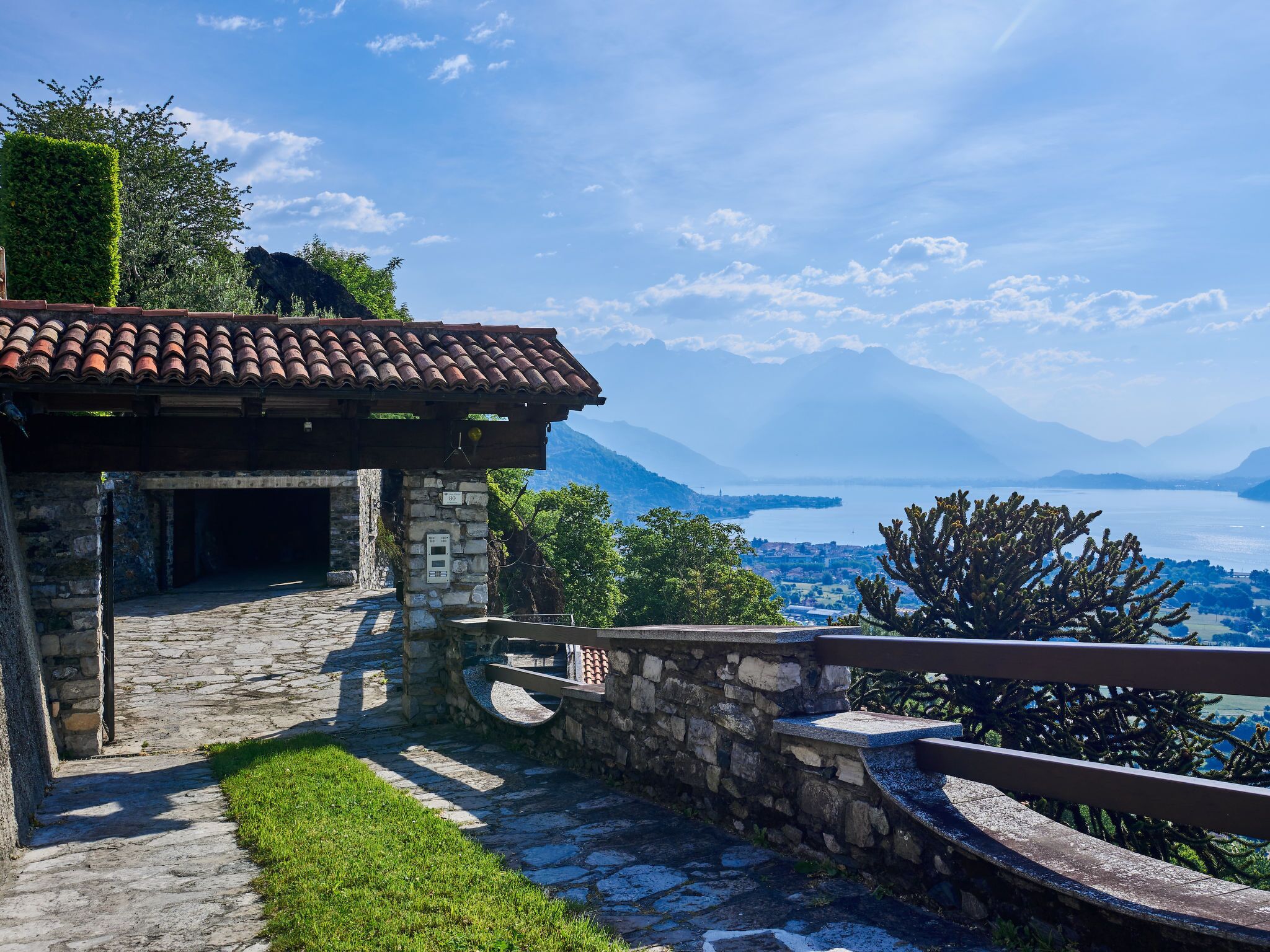 A stone building with a tiled roof, a stone staircase, and a view of a lake and mountains.