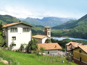 A rural village with a prominent white building featuring a bell tower, surrounded by lush green hills and a lake. - Apartment Nicole by Interhome (Porlezza)