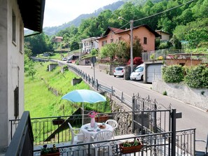 A balcony with a table set for dining, overlooking a road with cars and houses in a hilly area. - Apartment Nicole by Interhome (Porlezza)