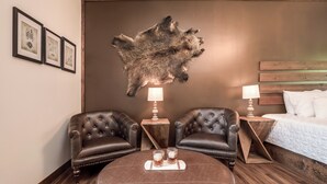 Une pièce comprenant deux fauteuils en cuir, un pouf rond, un lit avec une literie blanche et une grande peau de bête accrochée au mur.
