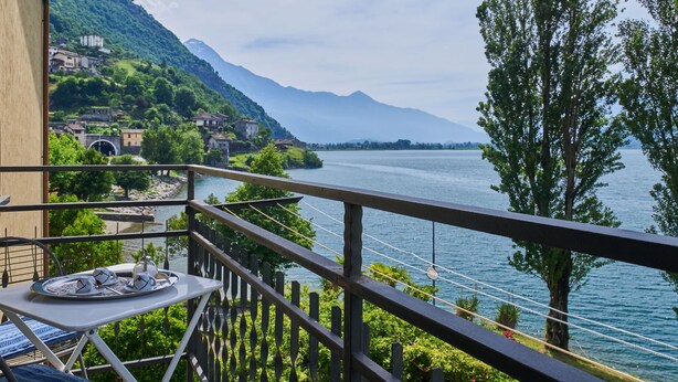 A balcony with a table and chairs, overlooking a lake with a mountain in the background. - Punto Lago by Interhome (Lago di Mezzola)