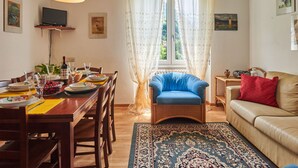 A dining area with a wooden table set for four, a blue armchair, a beige sofa, and a patterned rug. - Punto Lago by Interhome (Lago di Mezzola)