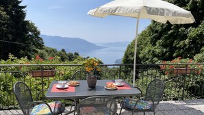 Une table avec un parasol blanc, une plante en pot, un croissant et une tasse, sur une terrasse dotée de chaises et offrant une vue sur les montagnes.