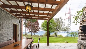 Une terrasse couverte avec une table et des bancs en bois, un sol en pierre et une vue sur un lac et des montagnes.