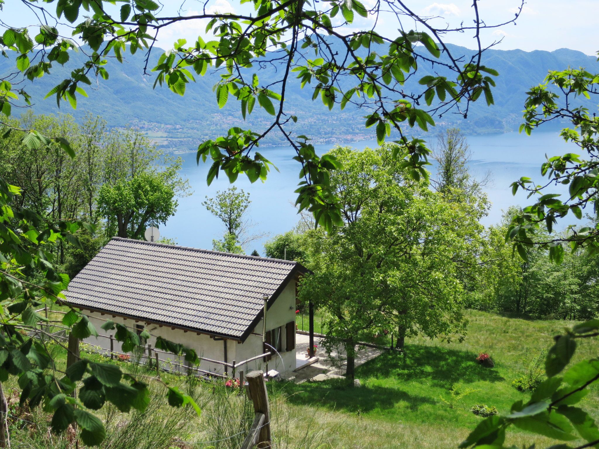 Una pequeña casa de techo con tejas, rodeada de exuberante vegetación y un lago al fondo.
