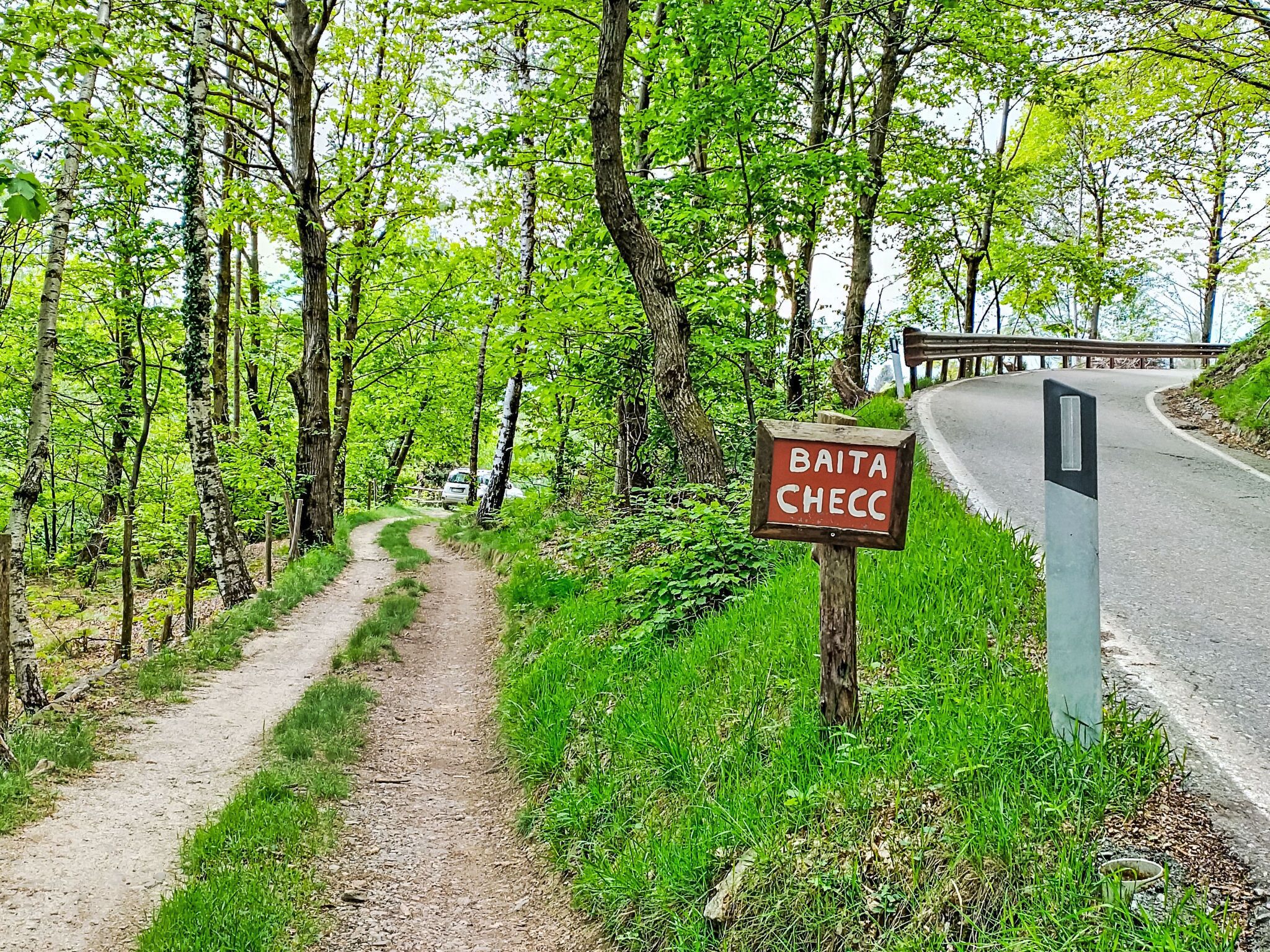 A forested area with a dirt path leading to a road. A sign reads 'BAITA CHECC.'