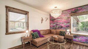 A cozy living room with a brown leather sofa, a round glass coffee table, and a vibrant floral wall mural.
